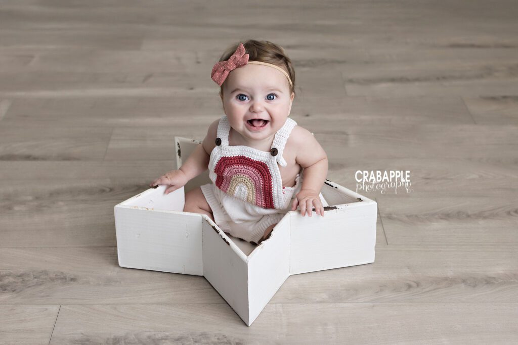 Six month old baby girl smiling in decorative star shaped bowl during milestone photography session
