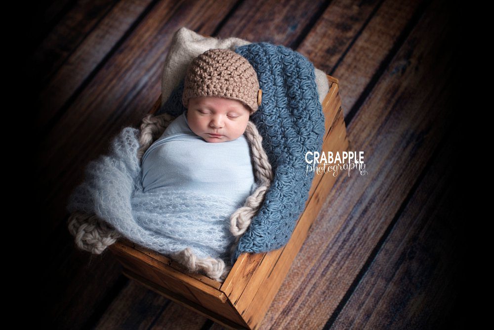 newborn baby boy portrait with dark brown wooden flooring, a lighter brown crate, different shades of blue blankets. Andover MA area newborn photographer