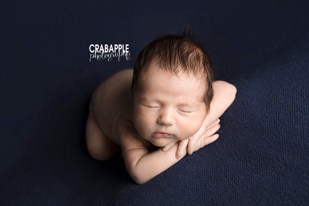 Baby boy with dark brown hair laying on a navy blue blanket. Andover MA Newborn photography.