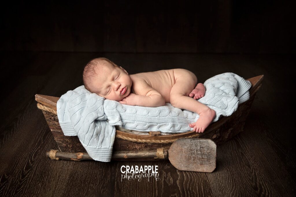 Newborn photos using a rustic wooden canoe as a prop.