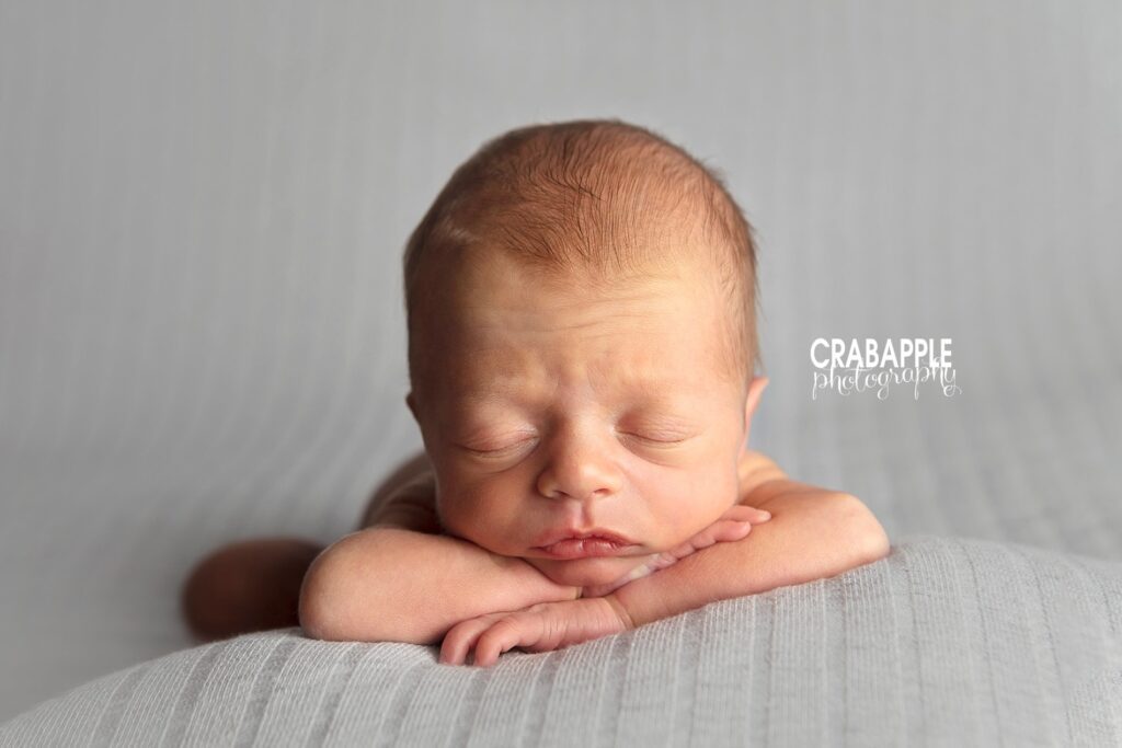 Simple newborn photo of a baby boy with head propped on his arms on a light gray blanket.