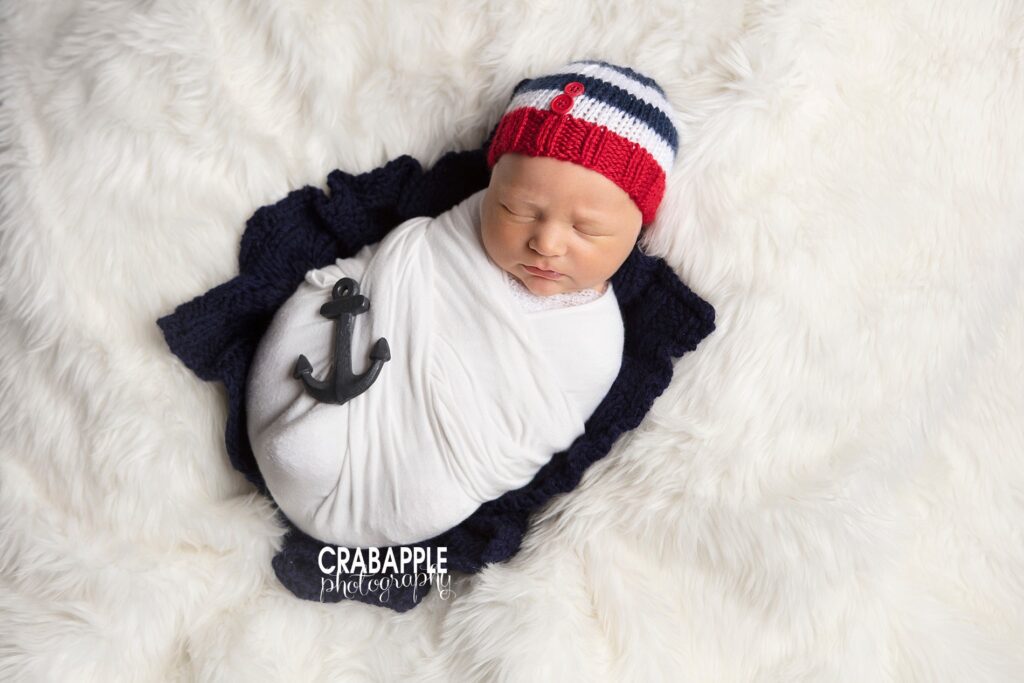 Nautical newborn portraits on a white fur with red, white, and blue knit hat and a small anchor.