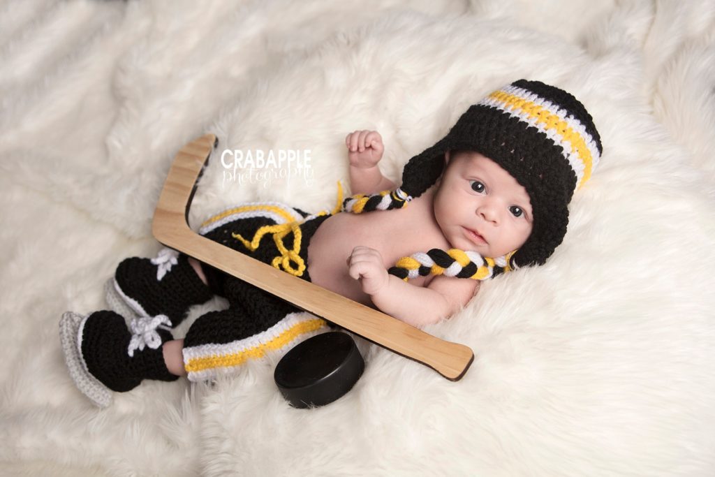 Boston Bruins themed newborn photo where a baby boy is laying on a white fur and wearing Bruins knit costume.