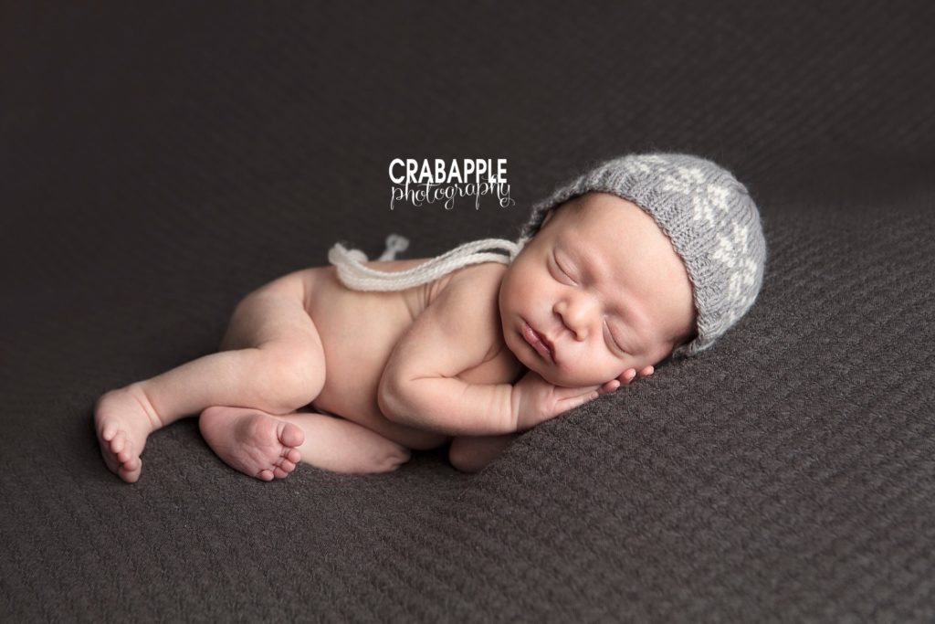 Sleeping newborn baby boy on a dark gray blanket wearing a knit fair isle hat.