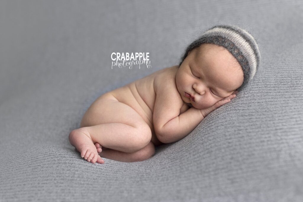 Simple gray newborn photo with a sleeping baby boy wearing a striped gray hat.