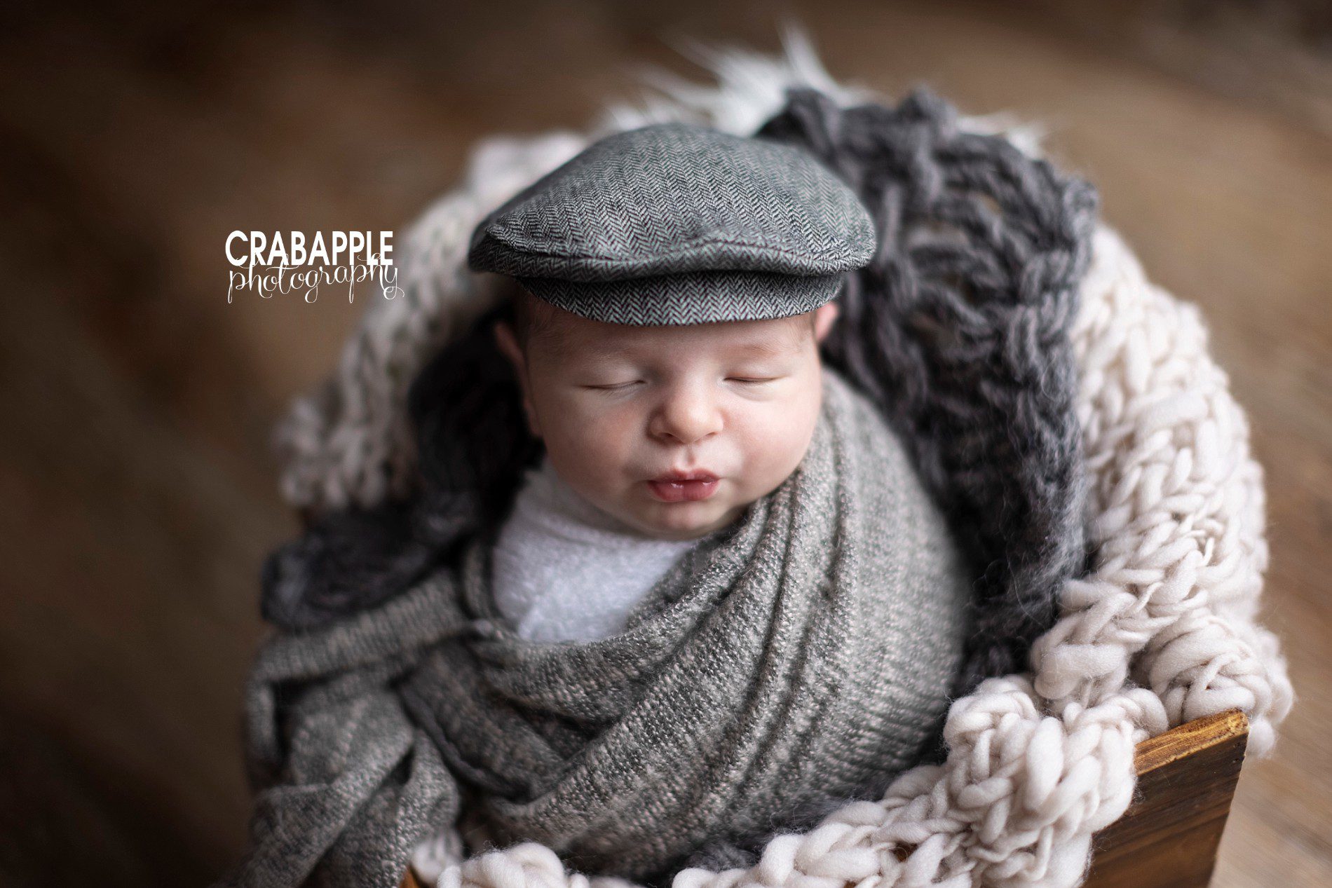 Newborn baby boy wearing a gray scally cap. He is surrounded by chunky knit blankets.