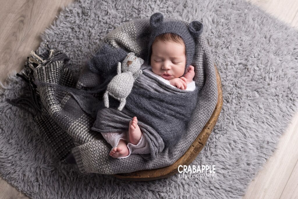 Newborn photo of a boy wrapped in gray sleeping on a gray blanket inside of a wooden prop. All of this is on a gray fur.
