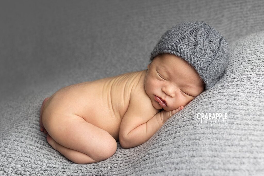 Simple and soft newborn photo ideas of newborn baby boy on his tummy on a gray blanket wearing a gray knit hat.