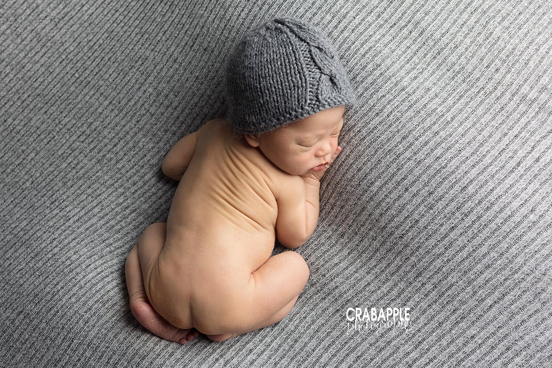 Simple and soft newborn photo ideas of newborn baby boy on his tummy on a gray blanket wearing a gray knit hat taken from above.