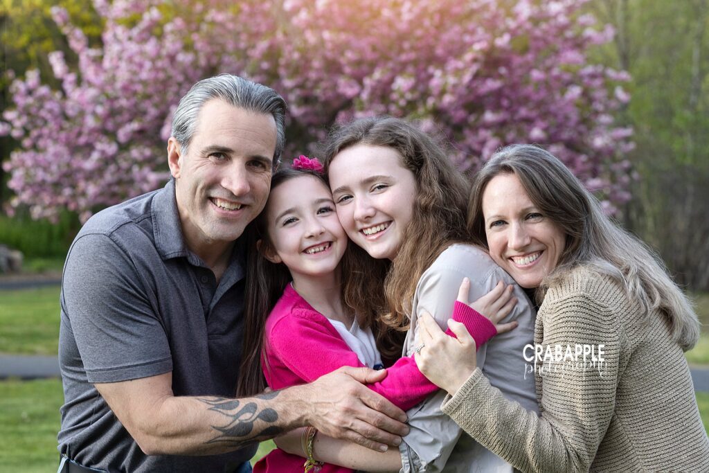 Portrait of a family all embracing, father and mother on either end with 14 and 8 year old daughters standing in between them.