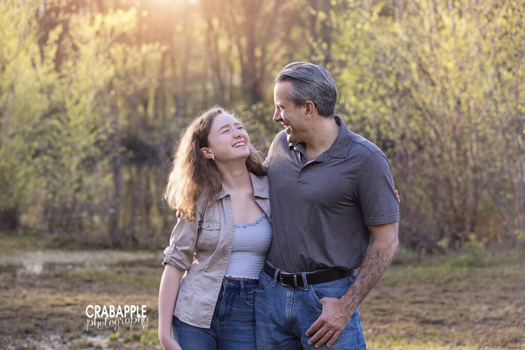 Family photos of laughing father and teenage daughter, standing with their arms around each other outside, looking at one another not the camera.