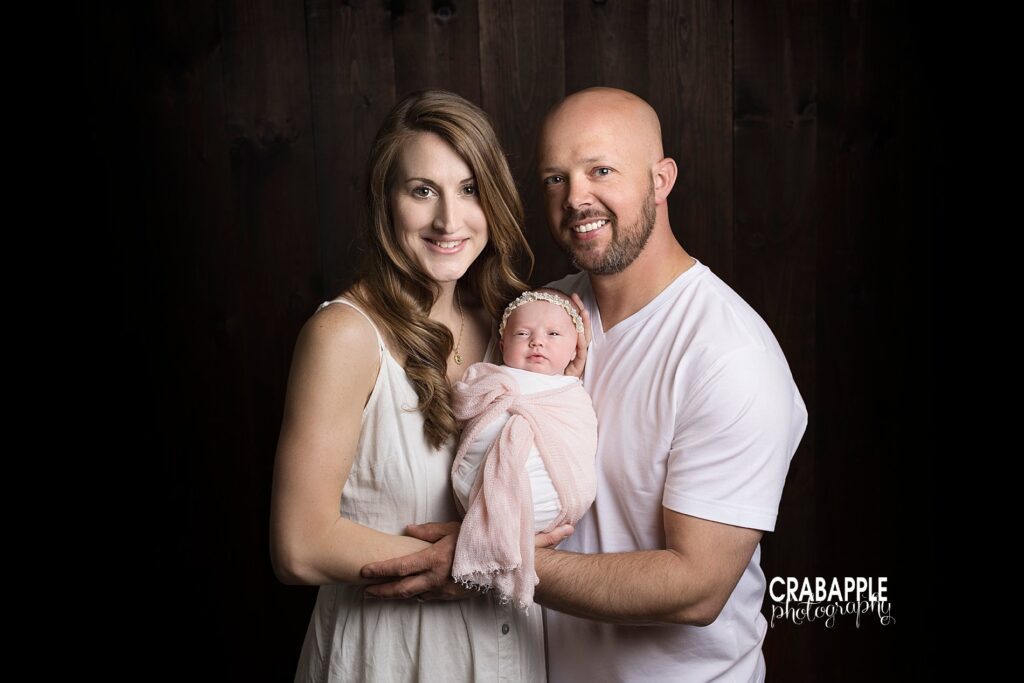 parent photos with newborn baby daughter in front of a black background.