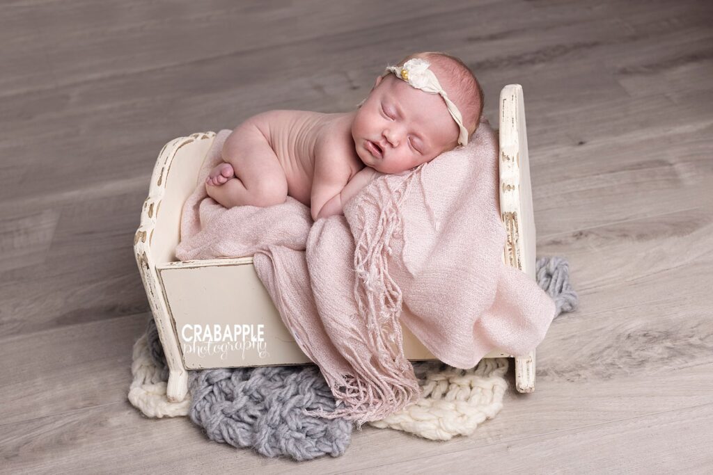 Newborn photos using vintage inspired wooden crib as a prop. White, gray, and blush pink blankets are included and a white headband.