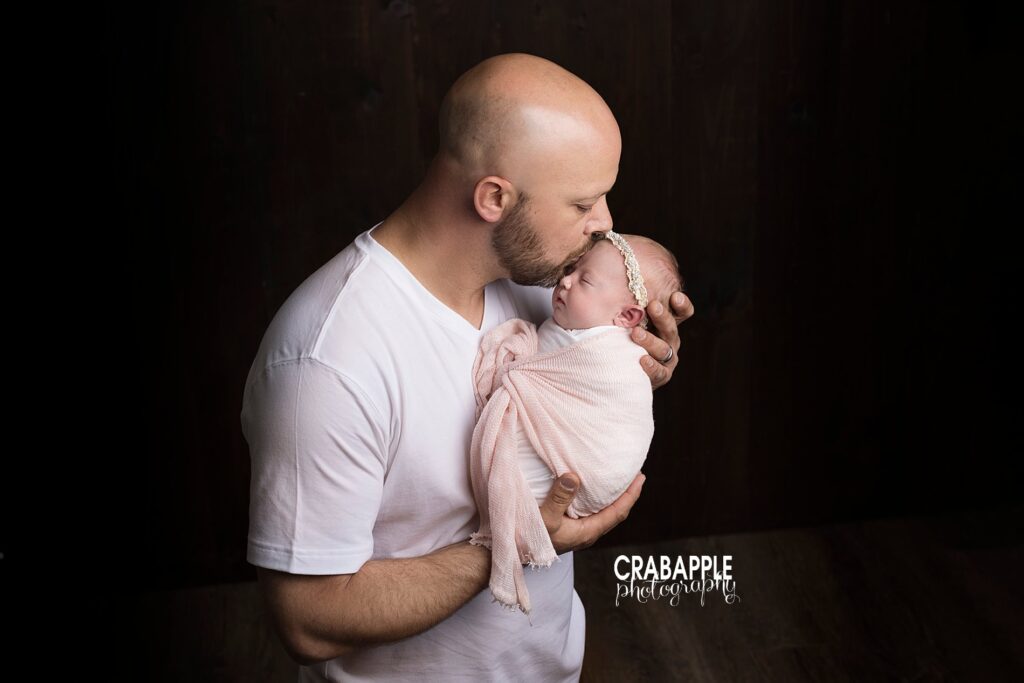 Father and daughter portraits of dad holding his newborn daughter and kissing her forehead.