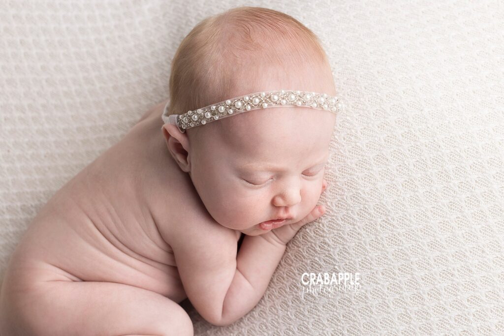 Clean, simple, serene newborn photos of baby girl on a cream blanket wearing a small vintage inspired pearl headband.