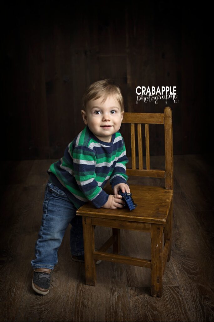 Vertical portrait of a one year old boy standing up holding onto a wooden chair.