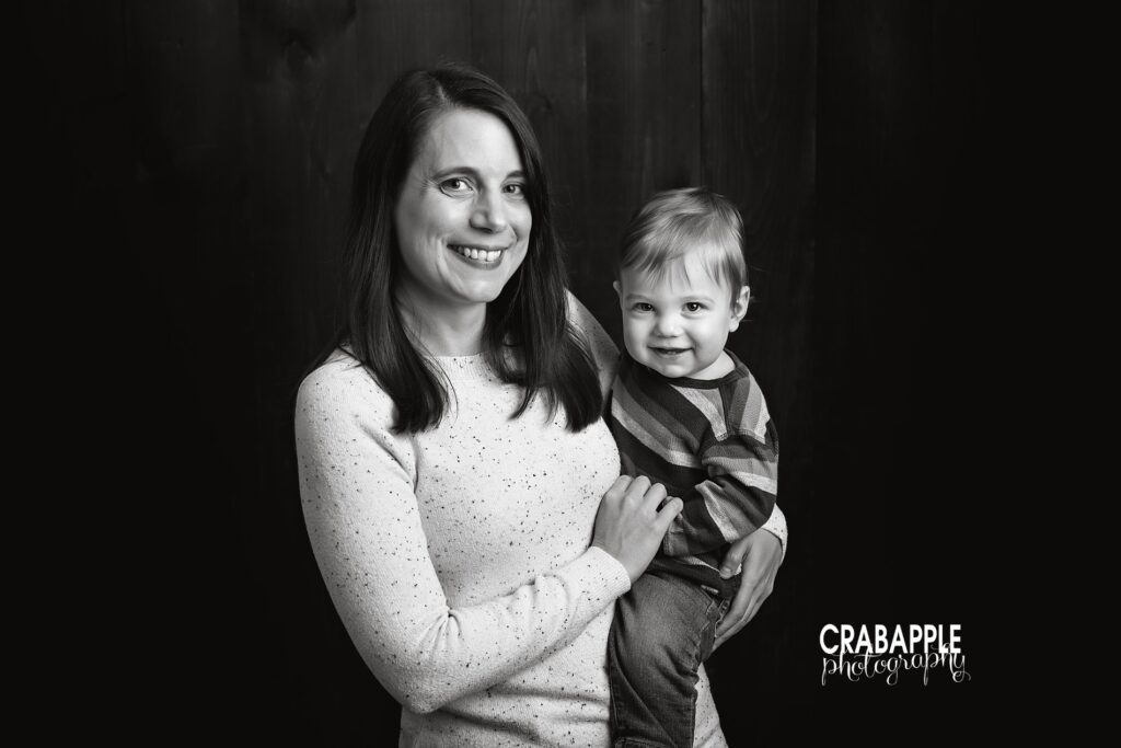 Black and white portrait of a mom holding her one year old son in front of a dark background.
