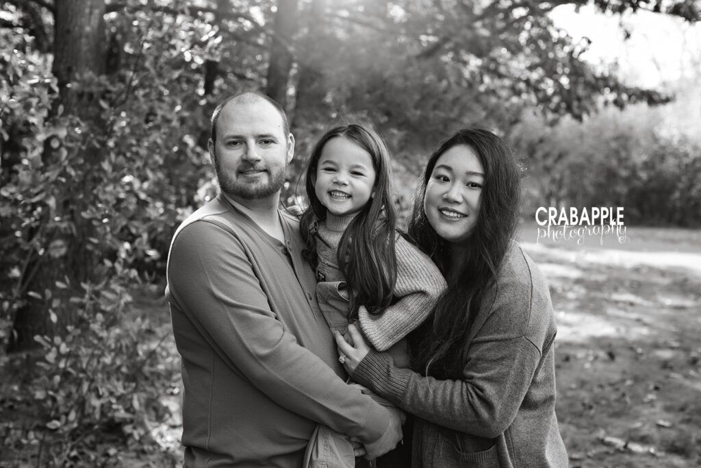 Black and white family portrait of mom, dad, and daughter outside during fall.