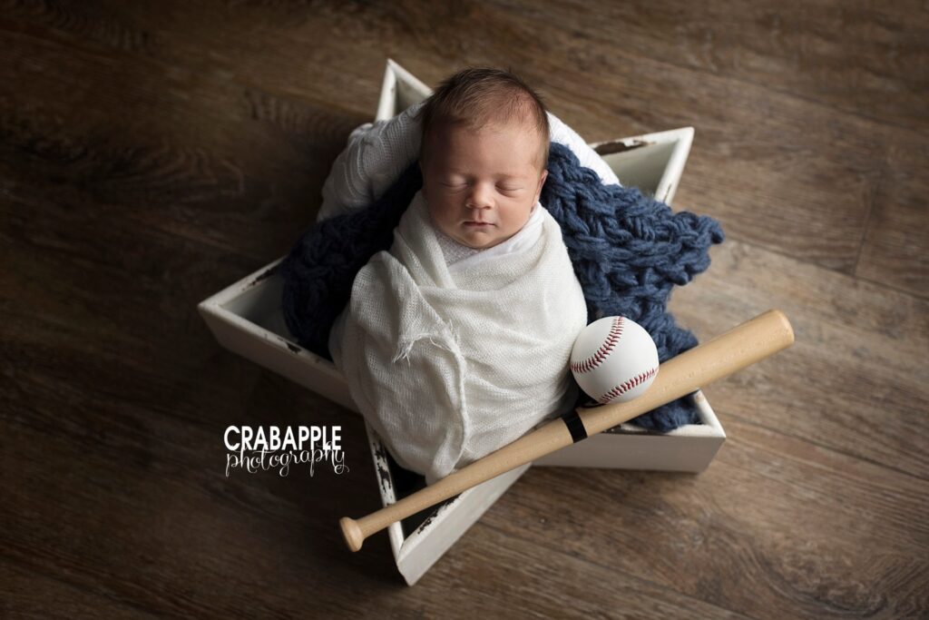 Newborn baby boy in a white wooden star prop with a baseball and baseball bat.