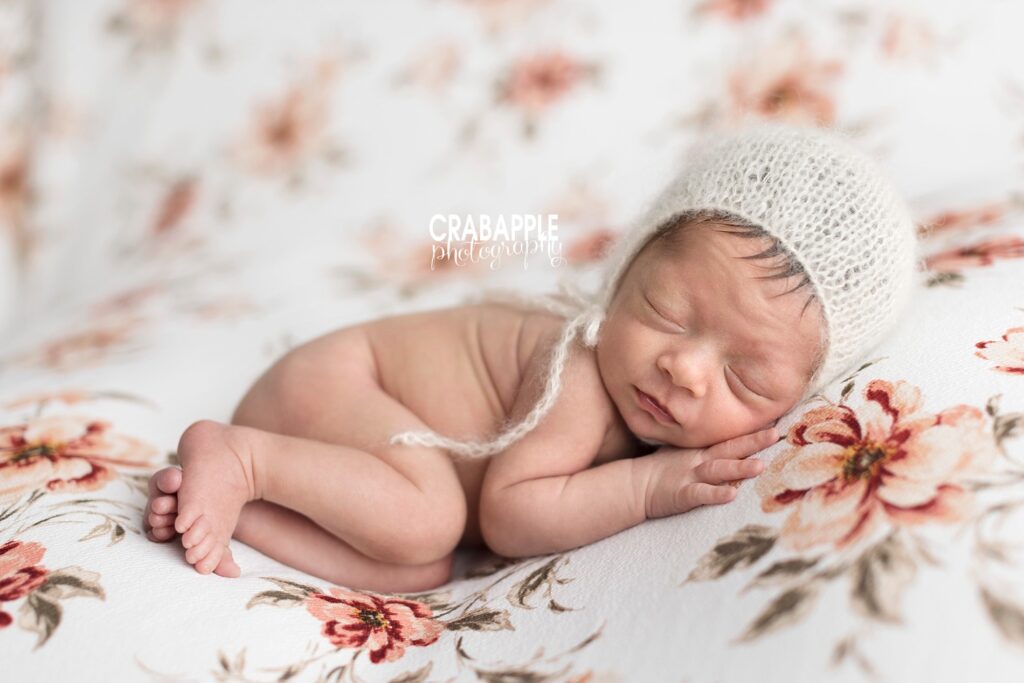 Newborn baby girl photos wearing a knit white bonnet on a floral blanket