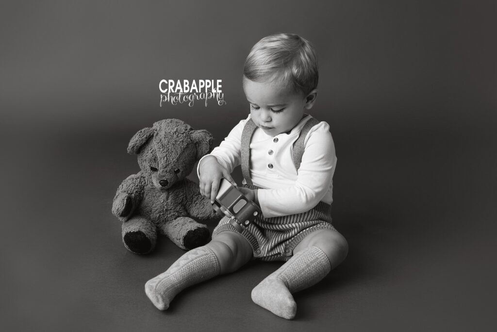 Classic and vintage inspired black and white toddler portrait of a two year old boy playing with a truck and sitting with a vintage teddy bear belonging to his dad.
