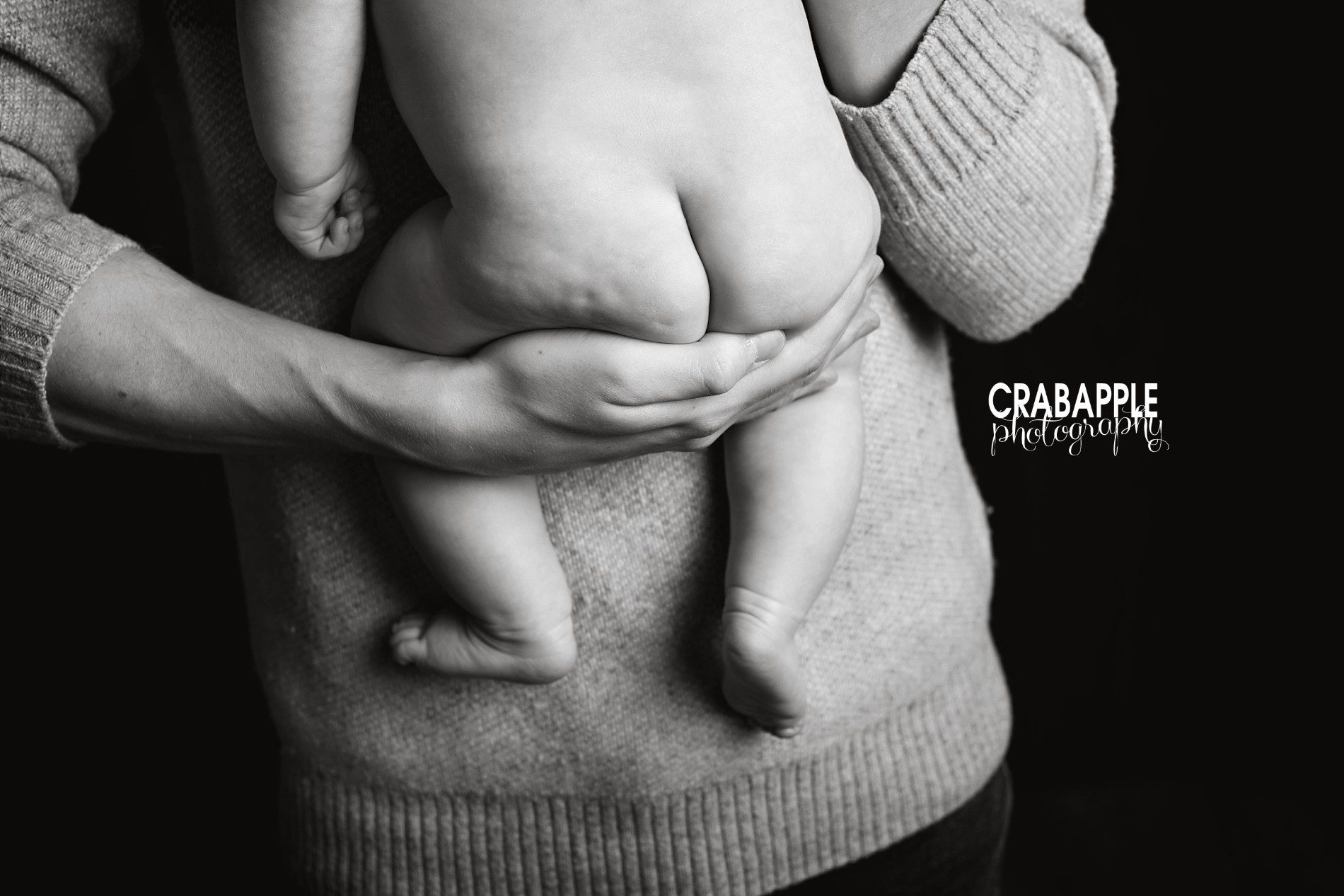 Black and white photo of a dad holding his son in his arms, showing son's bottom half and dad's hand and arm only.