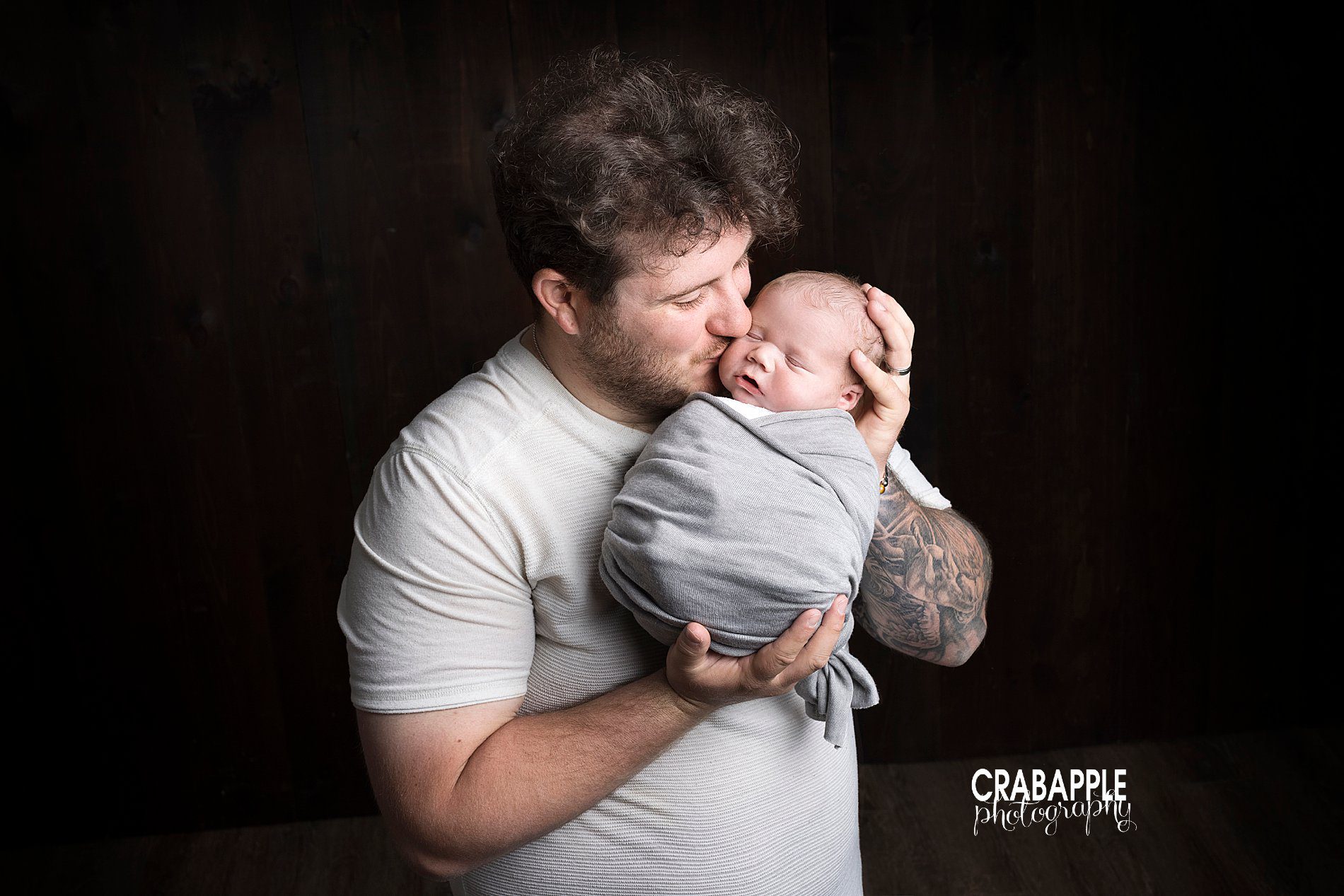 Portrait of father holding newborn son and kissing his cheek