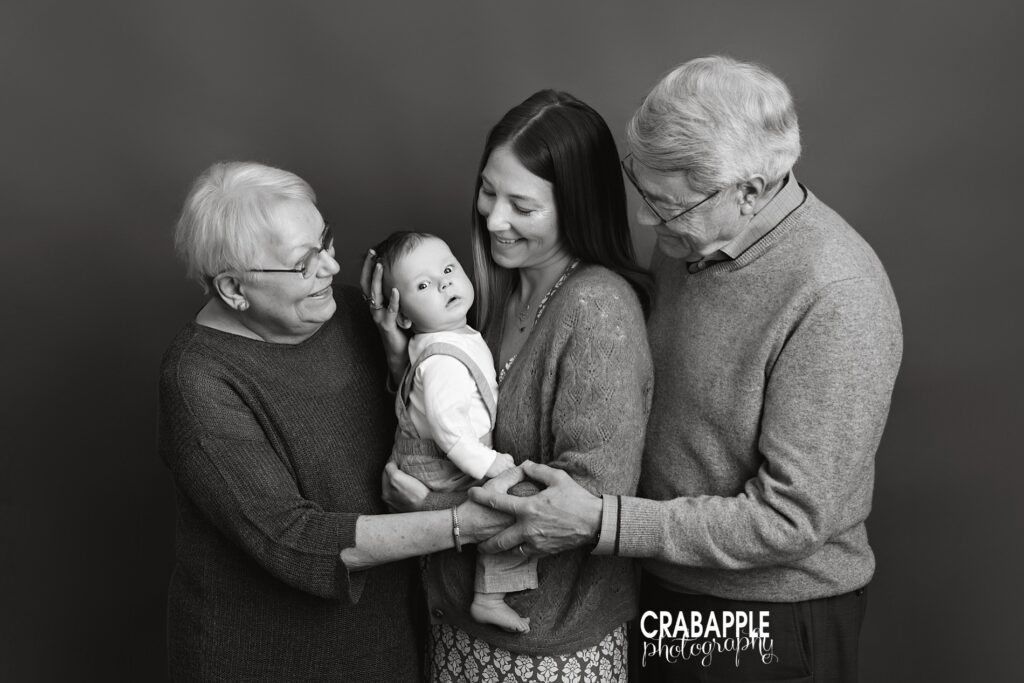 Black and white portraits of grandparents, mom, and baby. All the adults look at the baby while he looks at the camera.