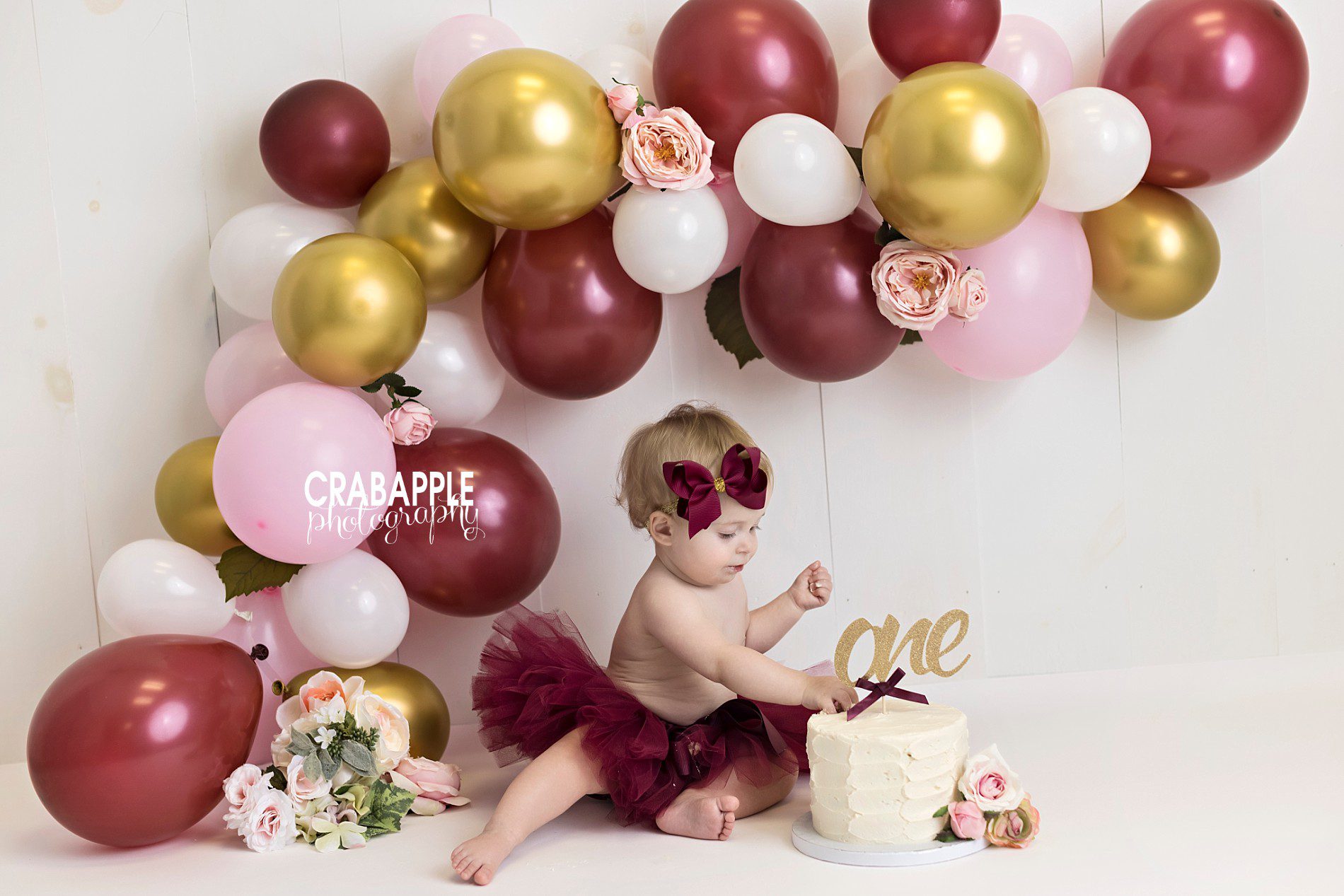 Pink, gold, red cake smash ideas with balloon arch and flowers.