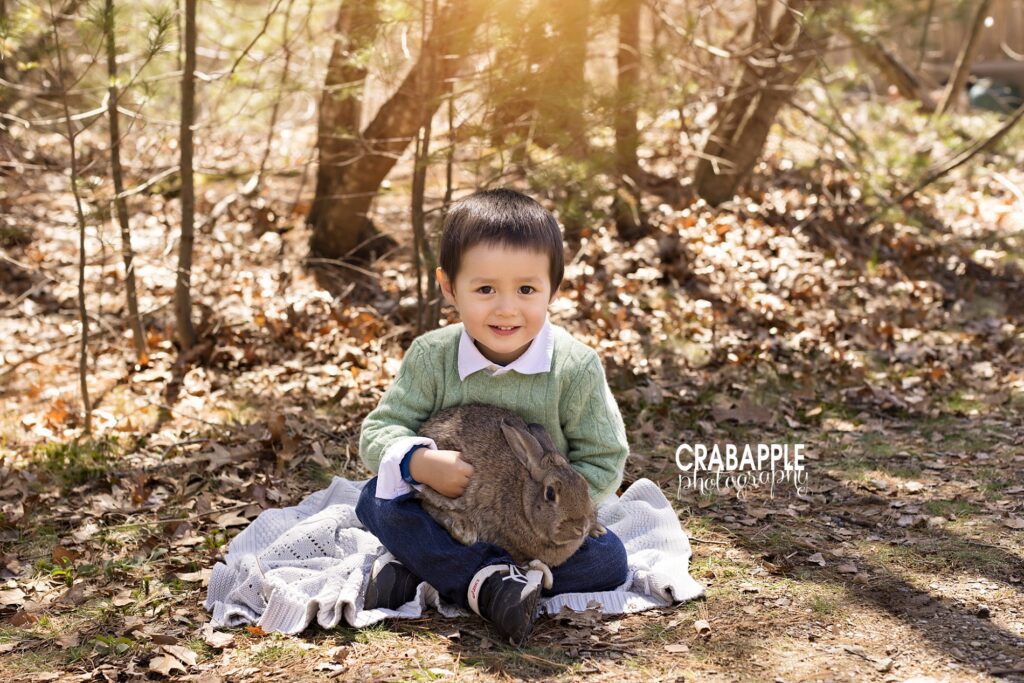 Child portraits of a young boy sitting on the ground outside holding a bunny rabbit.
