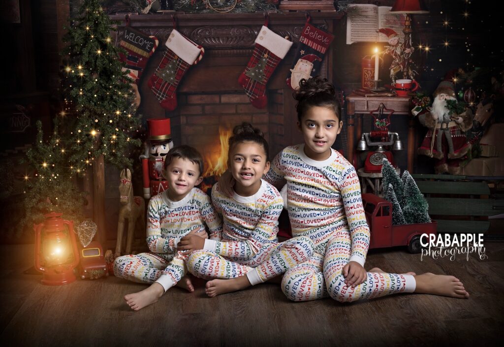 sibling photos of three children in matching pajamas in front of a Christmas themed fireplace set.