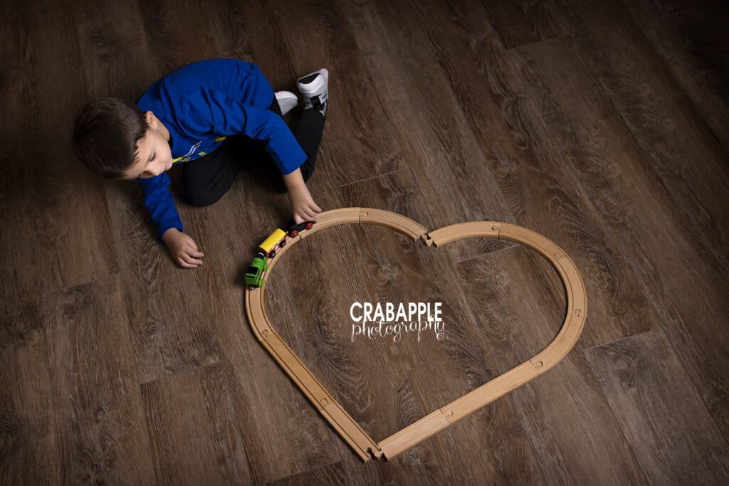 Favorite things child photo of a boy playing with a toy train, the tracks on the floor are in the shape of a heart.