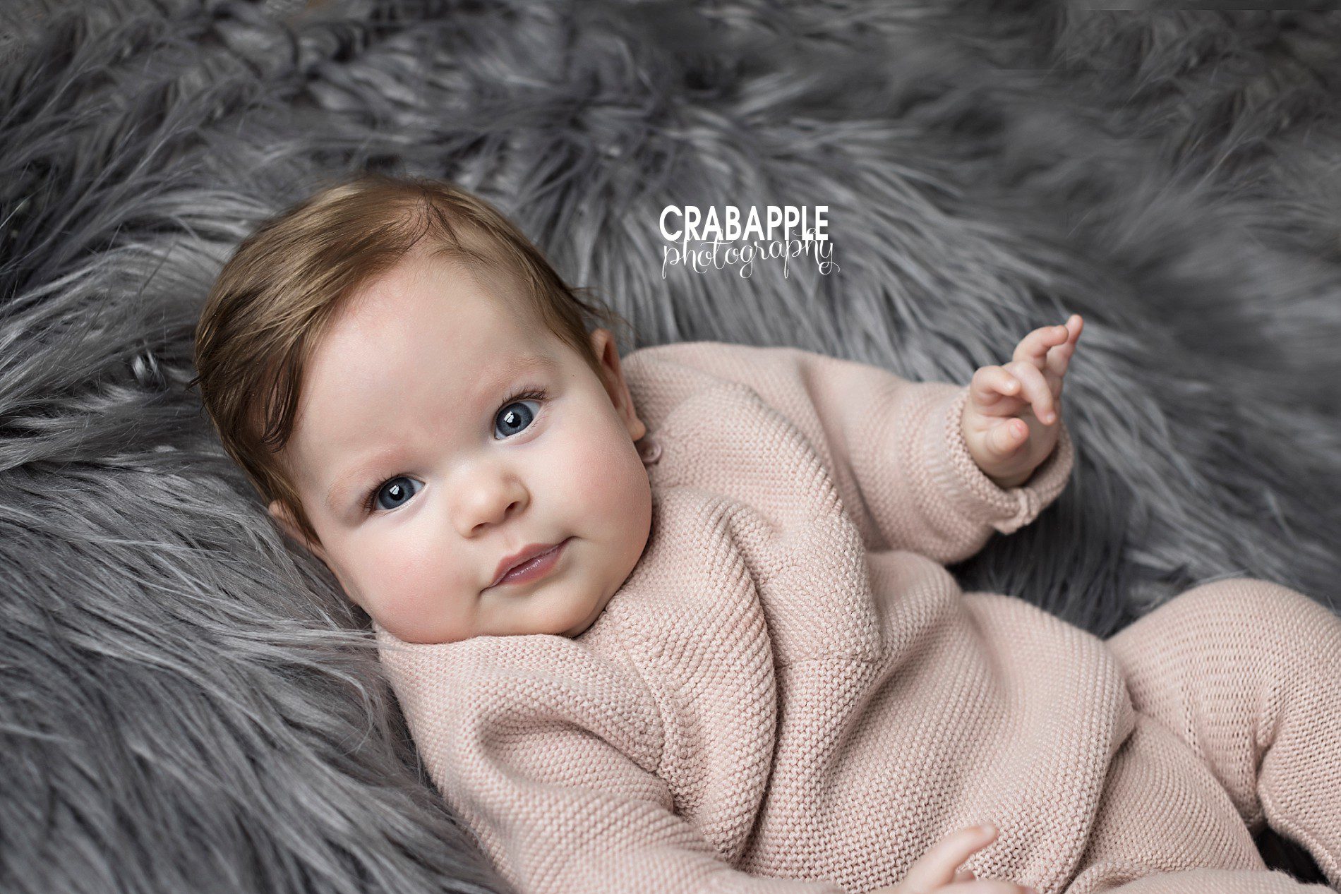 Baby portraits 6 month old baby girl in a light pink outfit on a gray fur.