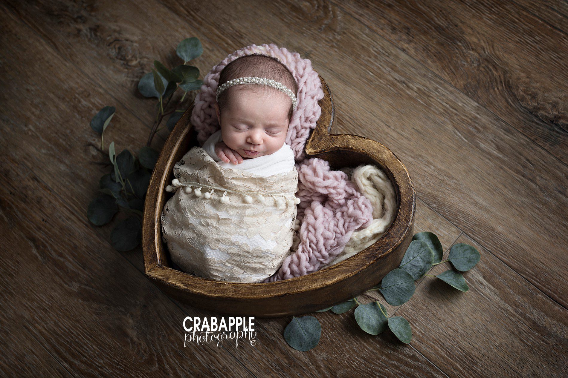 using props in newborn baby girl photos. Heart shaped wooden bowl for new baby photos. Faux eucalyptus leaves, lace, and chunky knit blankets.