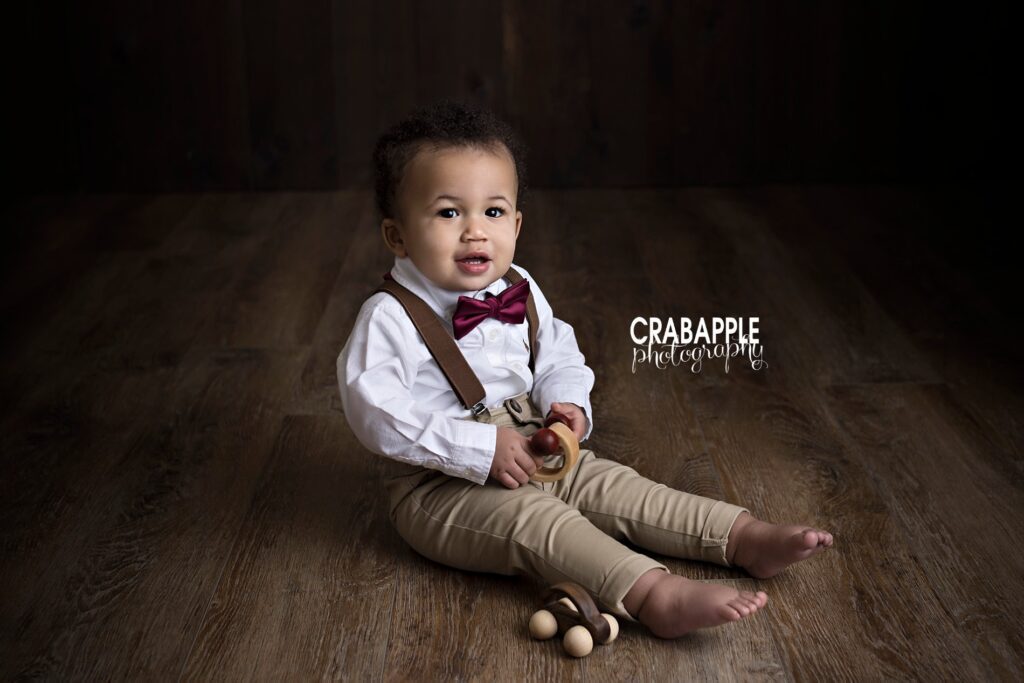1 year old Quincy MA baby boy in suspenders and bowtie during cake smash session