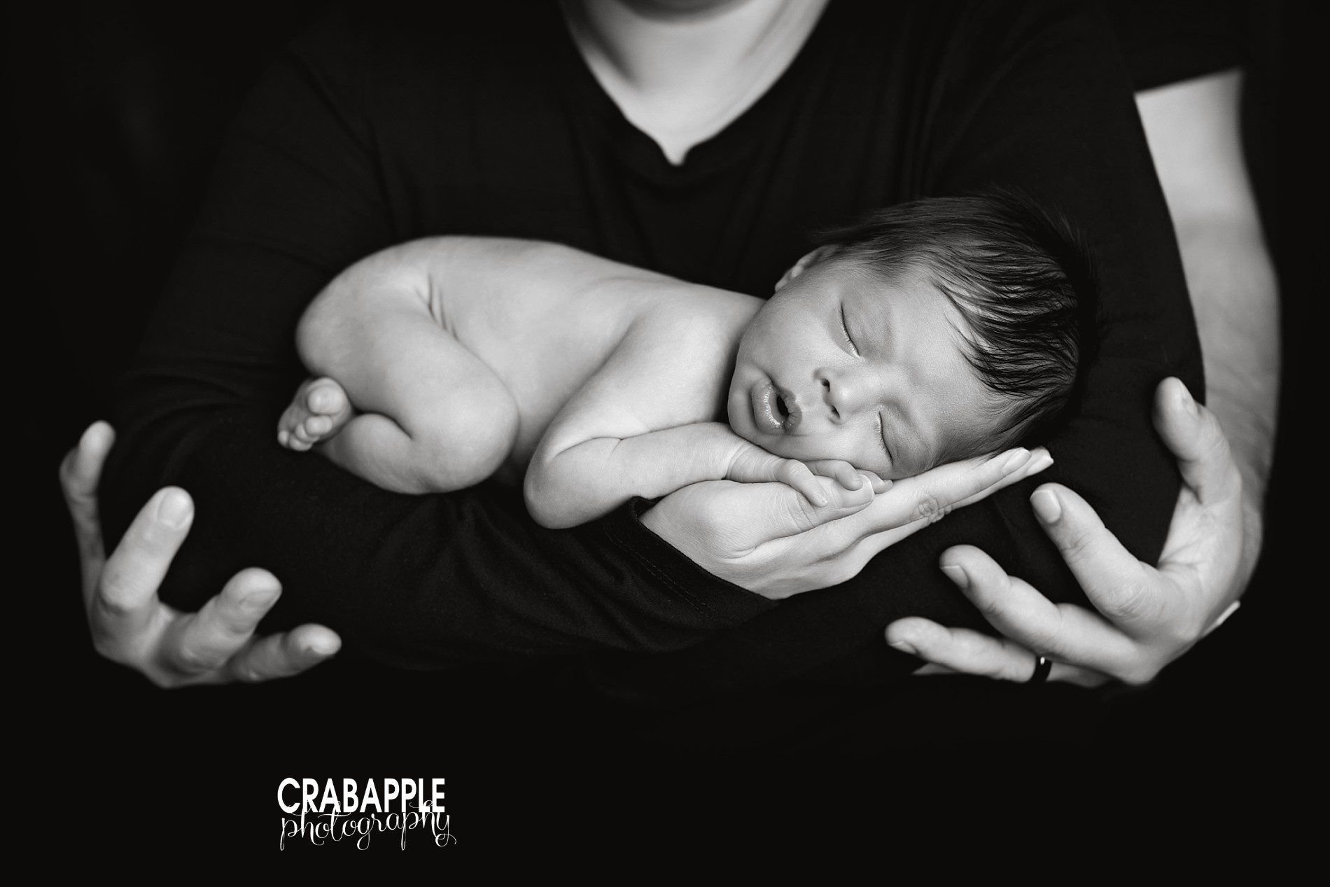 black and white newborn photo of baby boy held in mom's arms with dad's hands holding them both