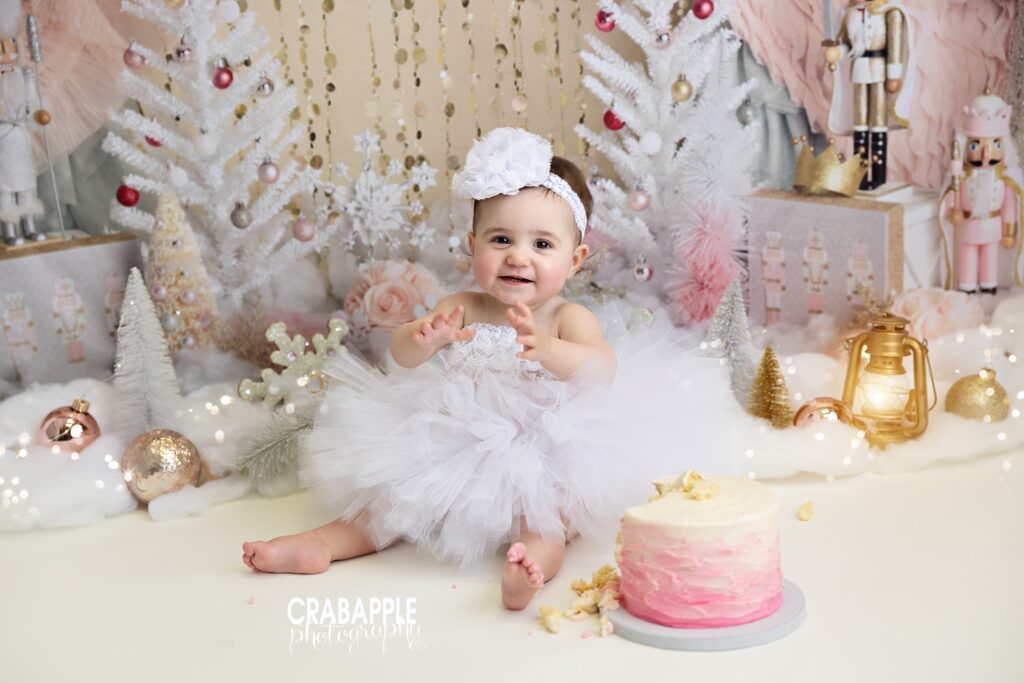 First birthday girl celebrating with pink and gold holiday cake smash setup
