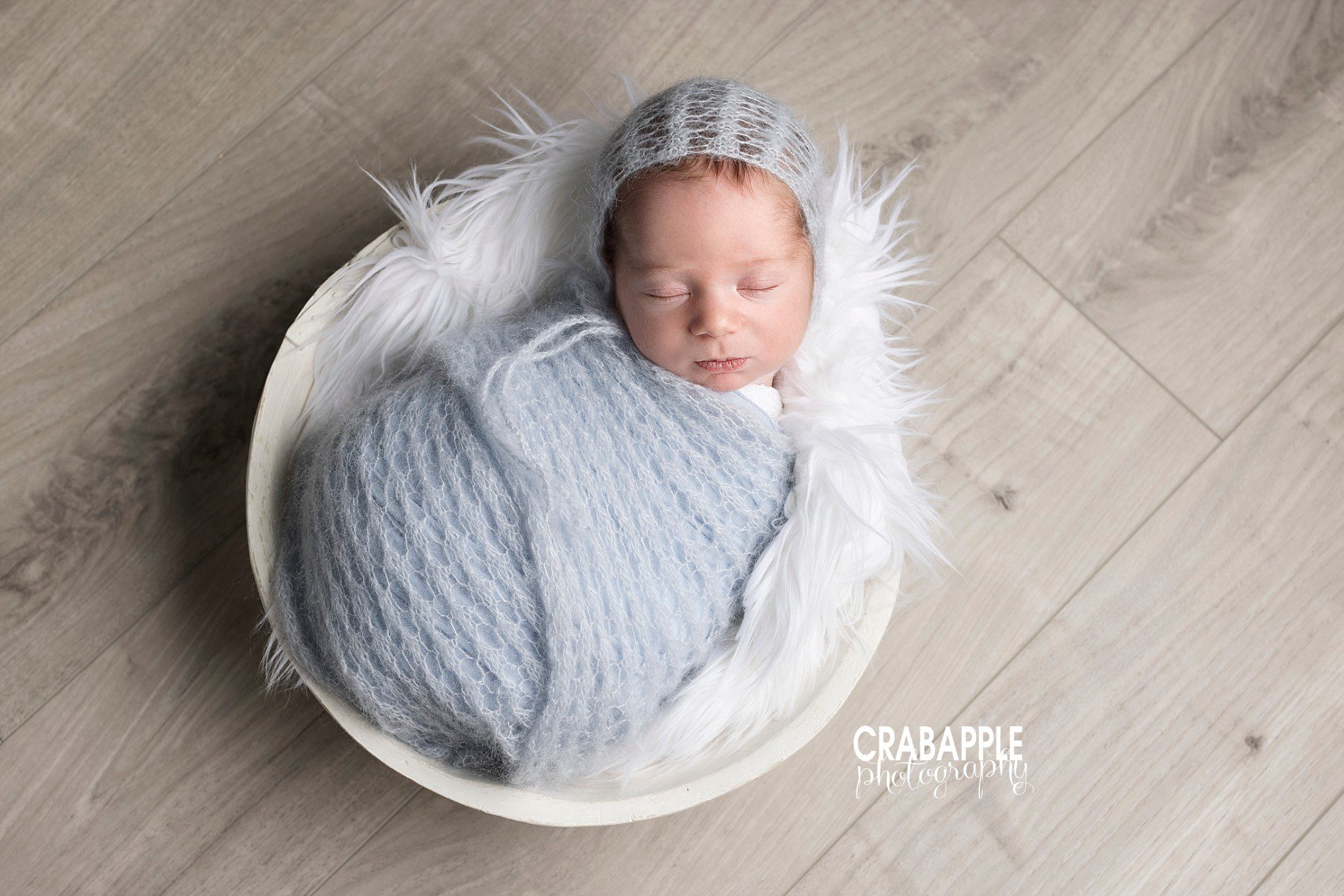 light blue and white newborn photo ideas using pastel blue swaddle and bonnet with white fur and light gray flooring