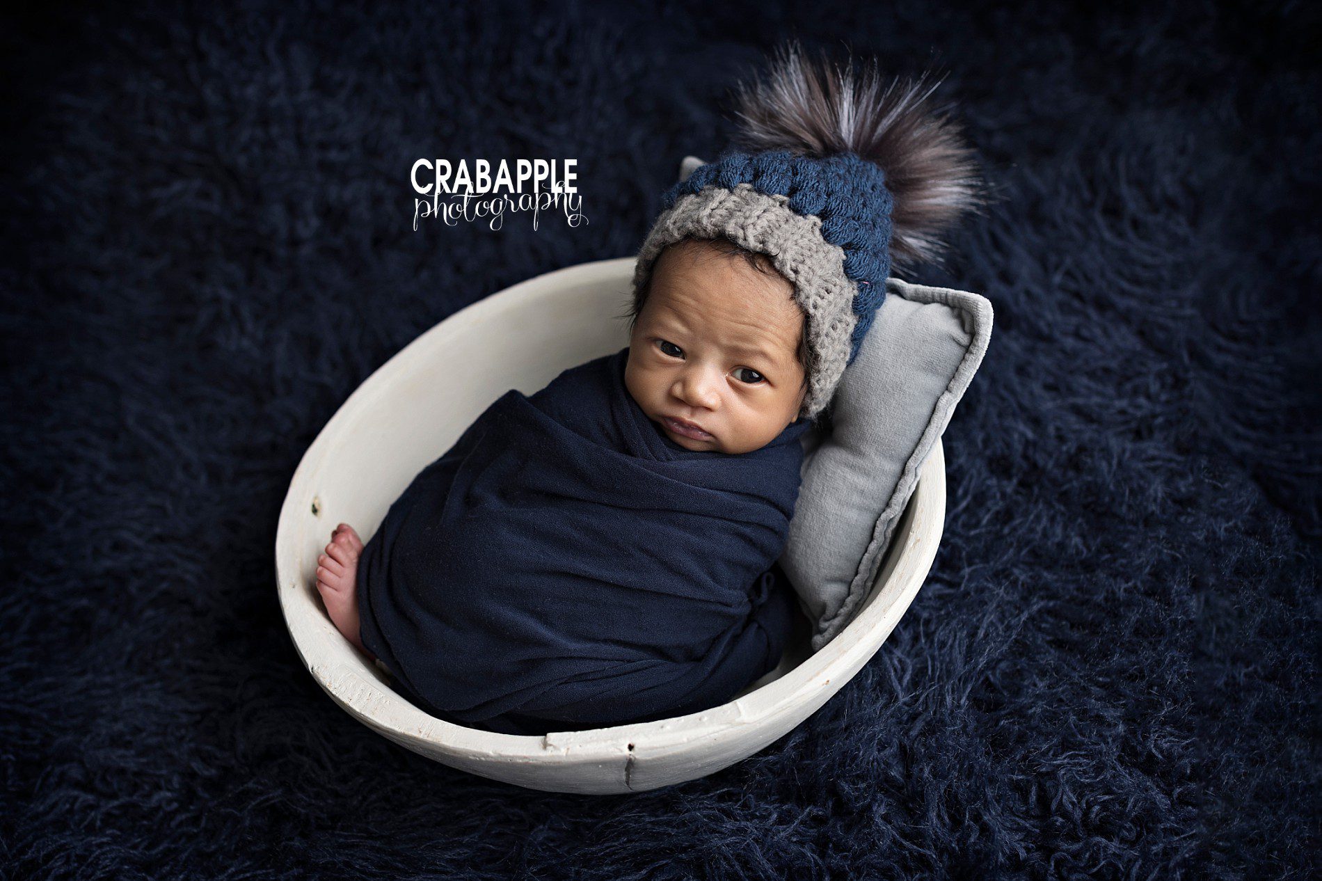 newborn photo ideas using navy blue fur, swaddle, and knit hat with white wooden bowl.