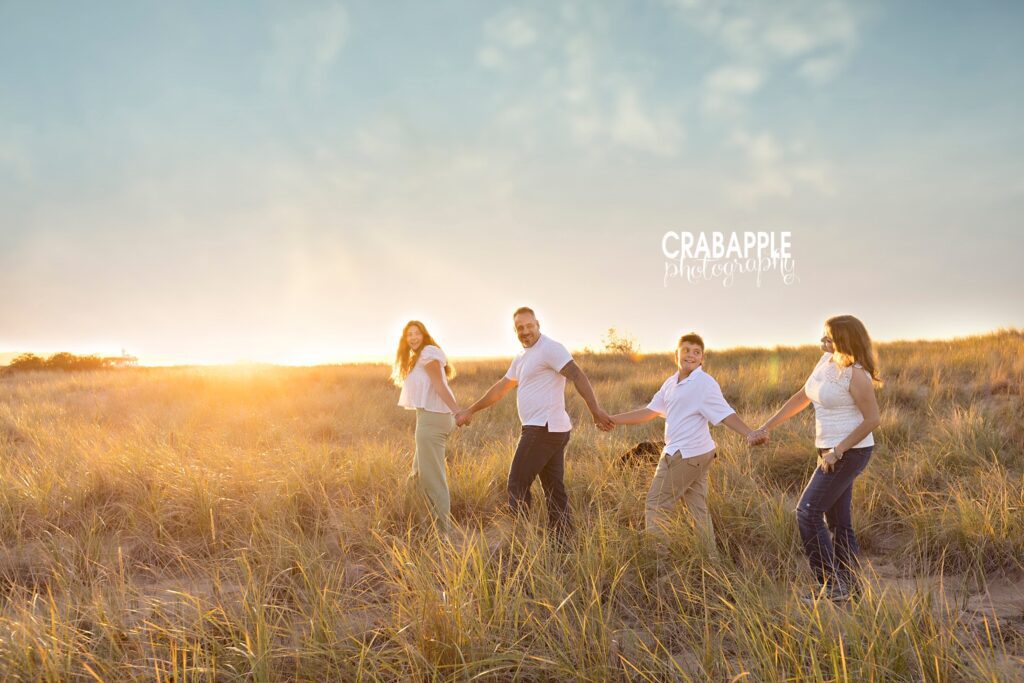 Family of four hold hands and walks with sunset behind them during golden hour beach photos