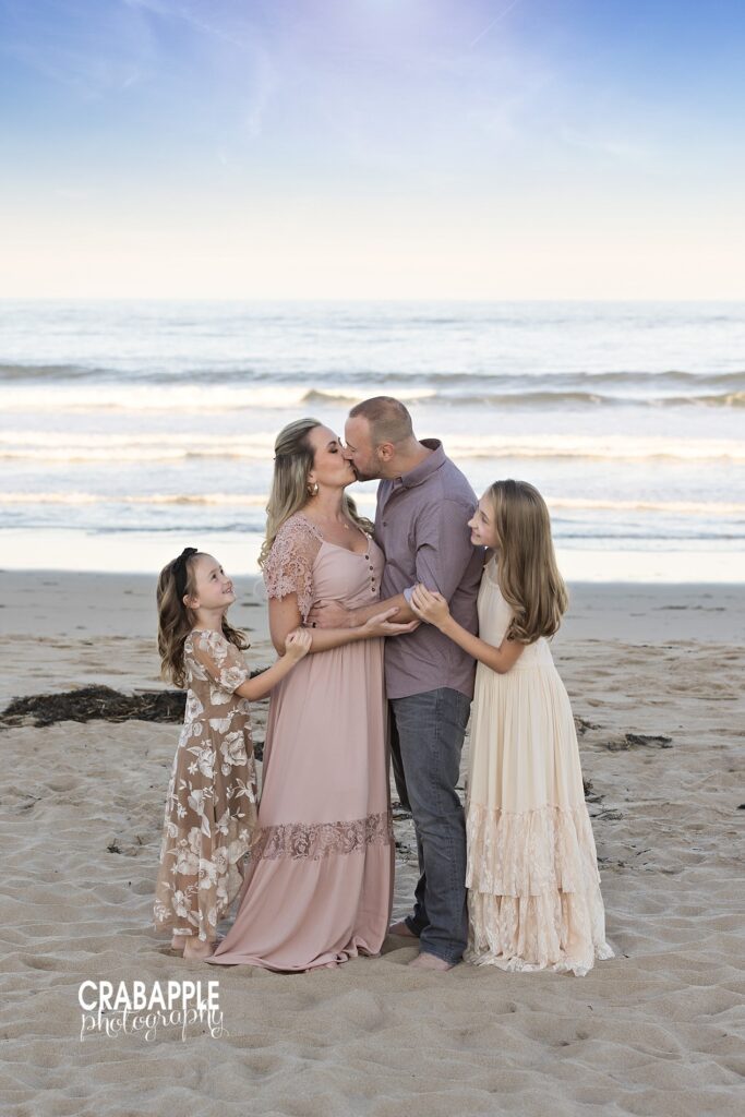 Mom and dad kiss while daughters watch on during beach family photos
