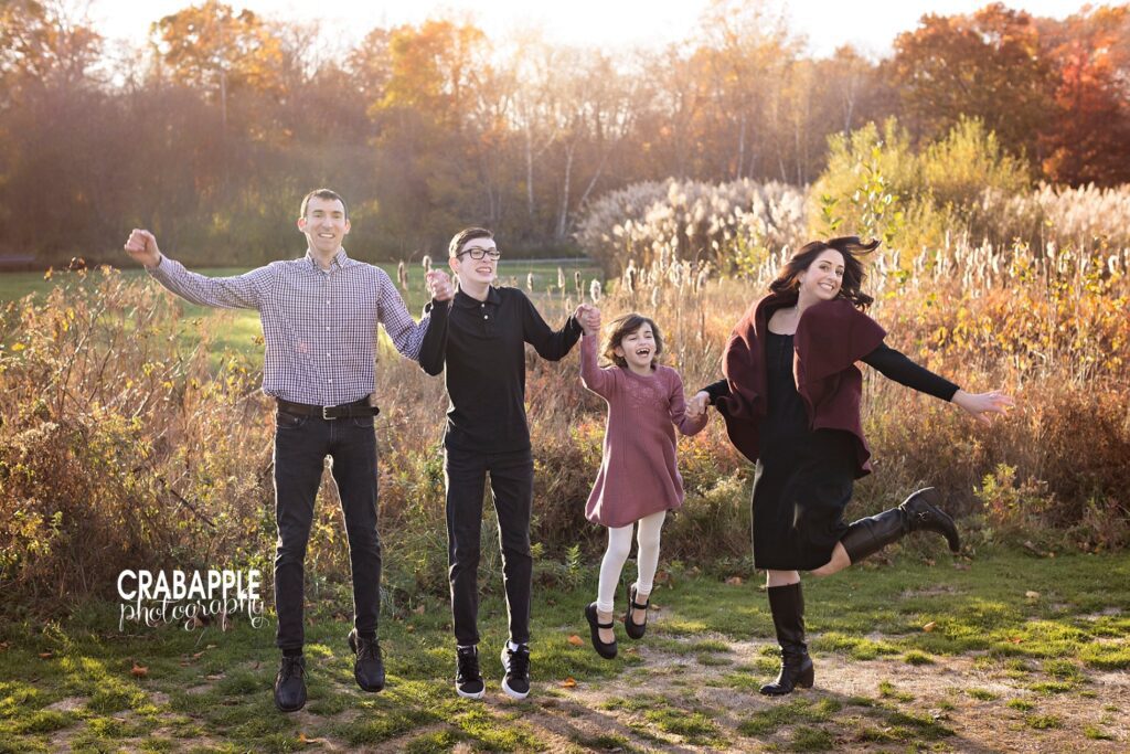 Mom, dad, and two children jump in front of a fall foliage back drop