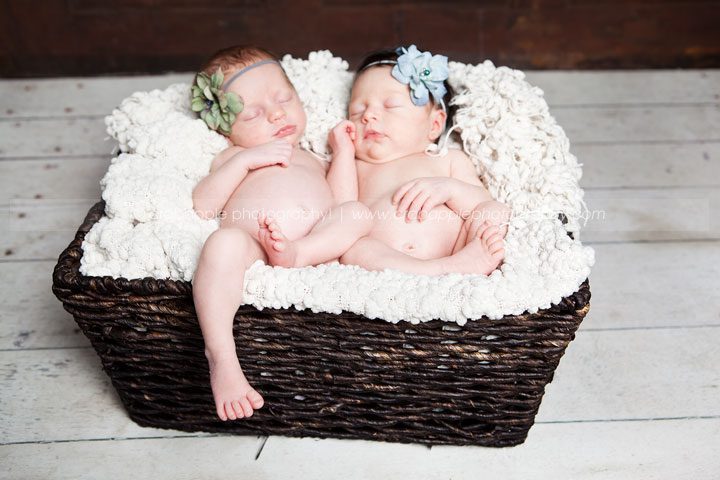 Newborn twins sleeping in a basket with matching purple and blue knit hats