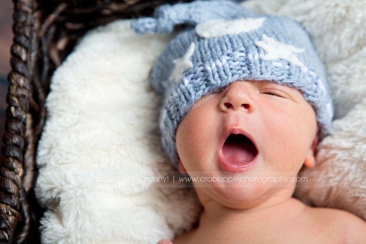 Yawning baby in light blue knit hat wrapped in white fur
