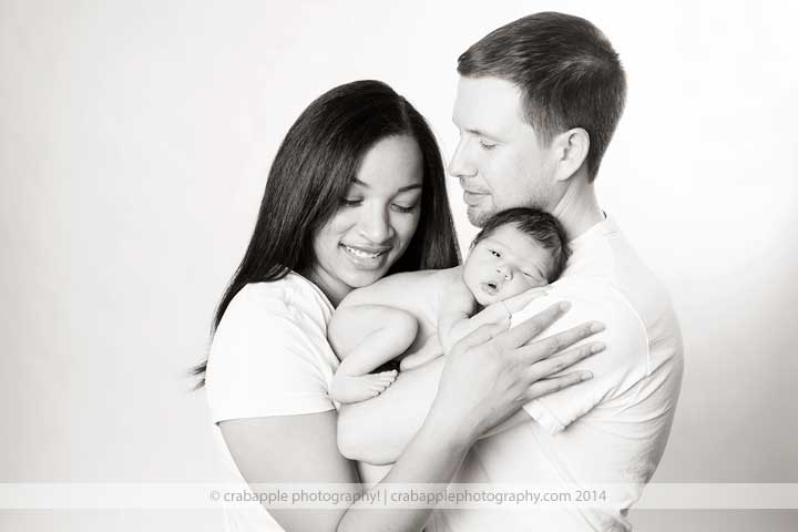 Black and white photo of parents holding their newborn baby and smiling softly, not looking at camera