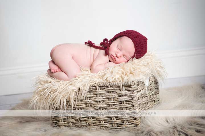 Newborn baby girl in burgundy headband sleeping in a wicker basket 