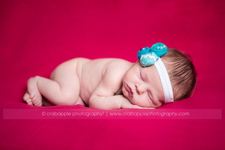 Newborn girl with teal and pink flower headband sleeping on hot pink background