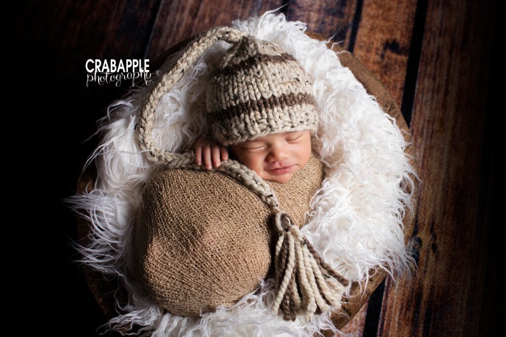 Newborn wrapped in rustic fur and hat posed in a wooden bucket 
