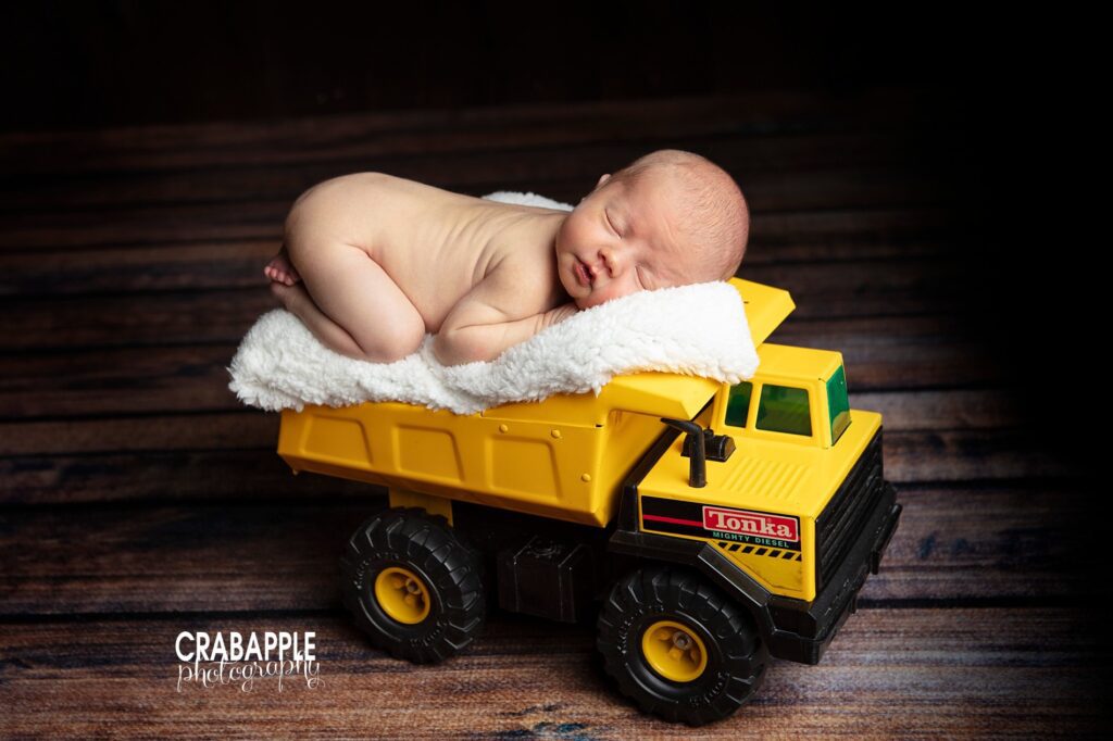 Newborn sleeping on yellow toy dump truck 

