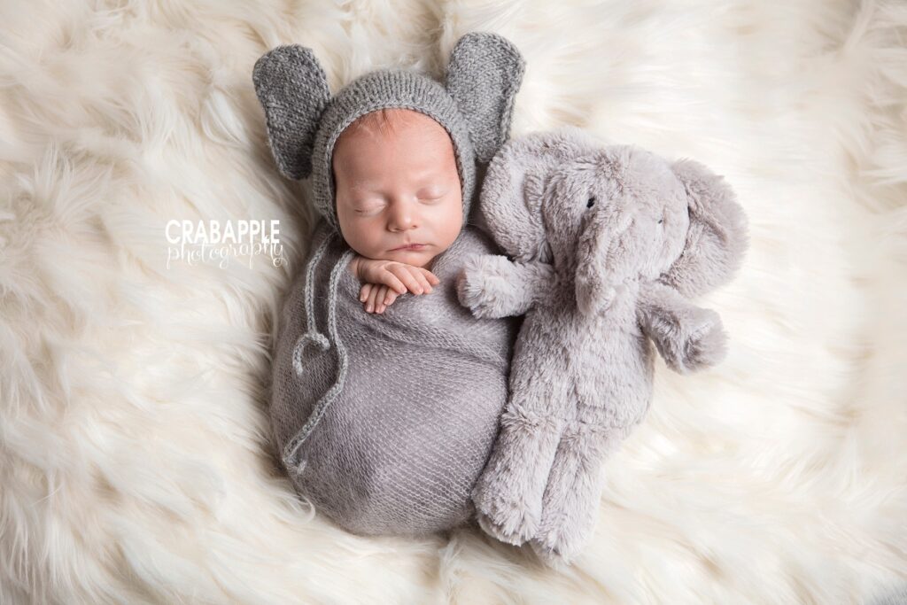 Baby in knit hat cuddled next to stuffed elephant 